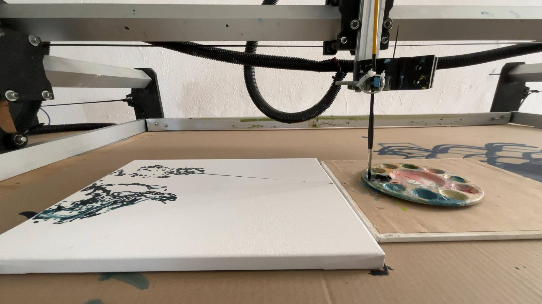 Plotter with brush head and paint palette beside a canvas