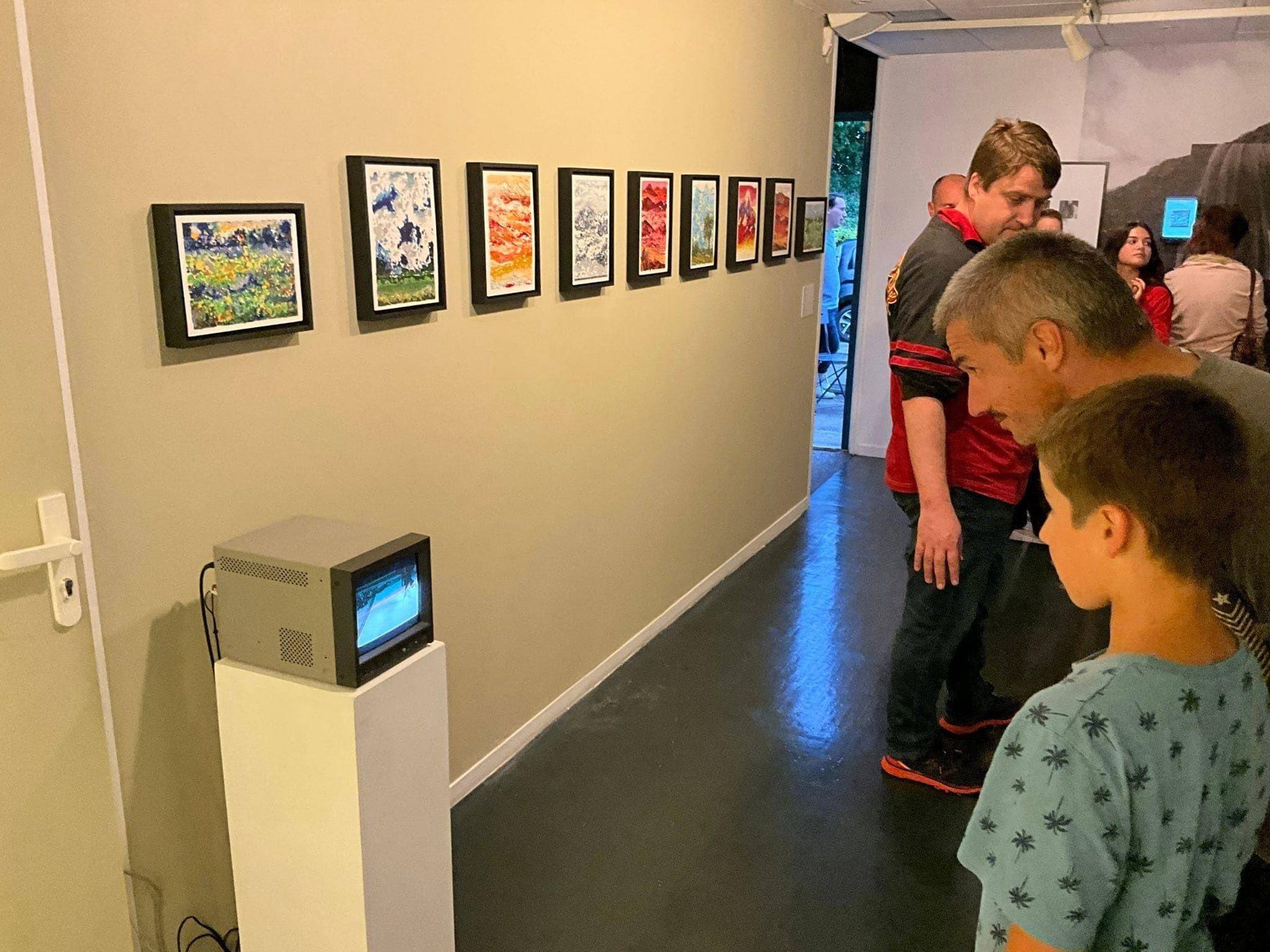 Visitors looking at a row of small paintings