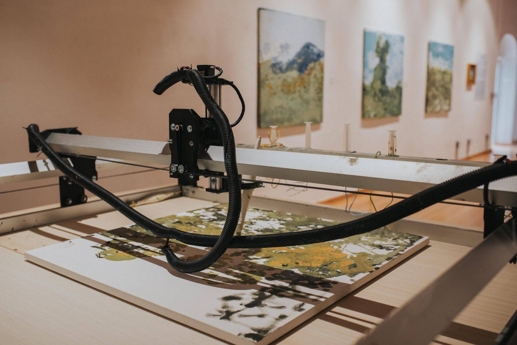 The plotter painting inside the museum gallery, with finished paintings on the wall